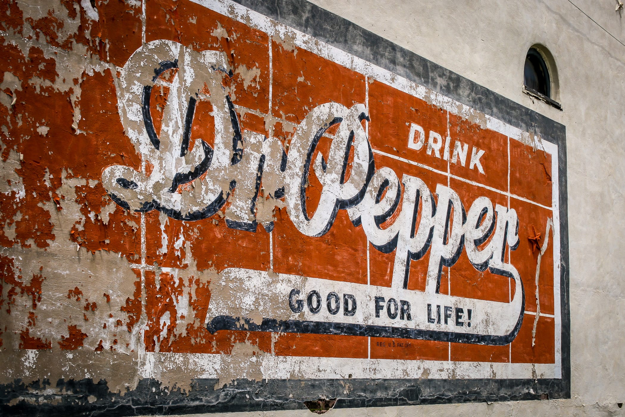 A cracked and fading Dr Pepper sign on the side of a decaying building in Downtown Pilot Point, Texas.