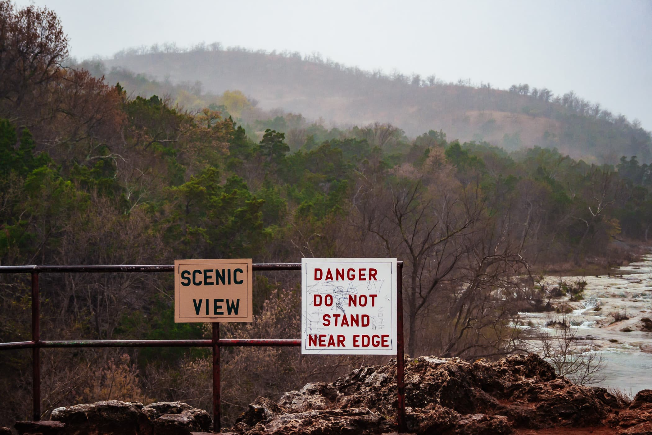 A warning sign at Turner Falls in Oklahoma on an overcast day.