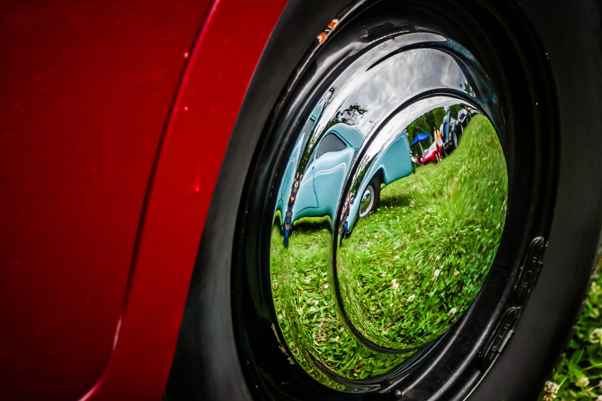 Classic cars (and, if you look closely, the photographer) reflected in the polished chrome wheel of a Sunbeam Talbot 90 at Dallas' All British and European Car Day.