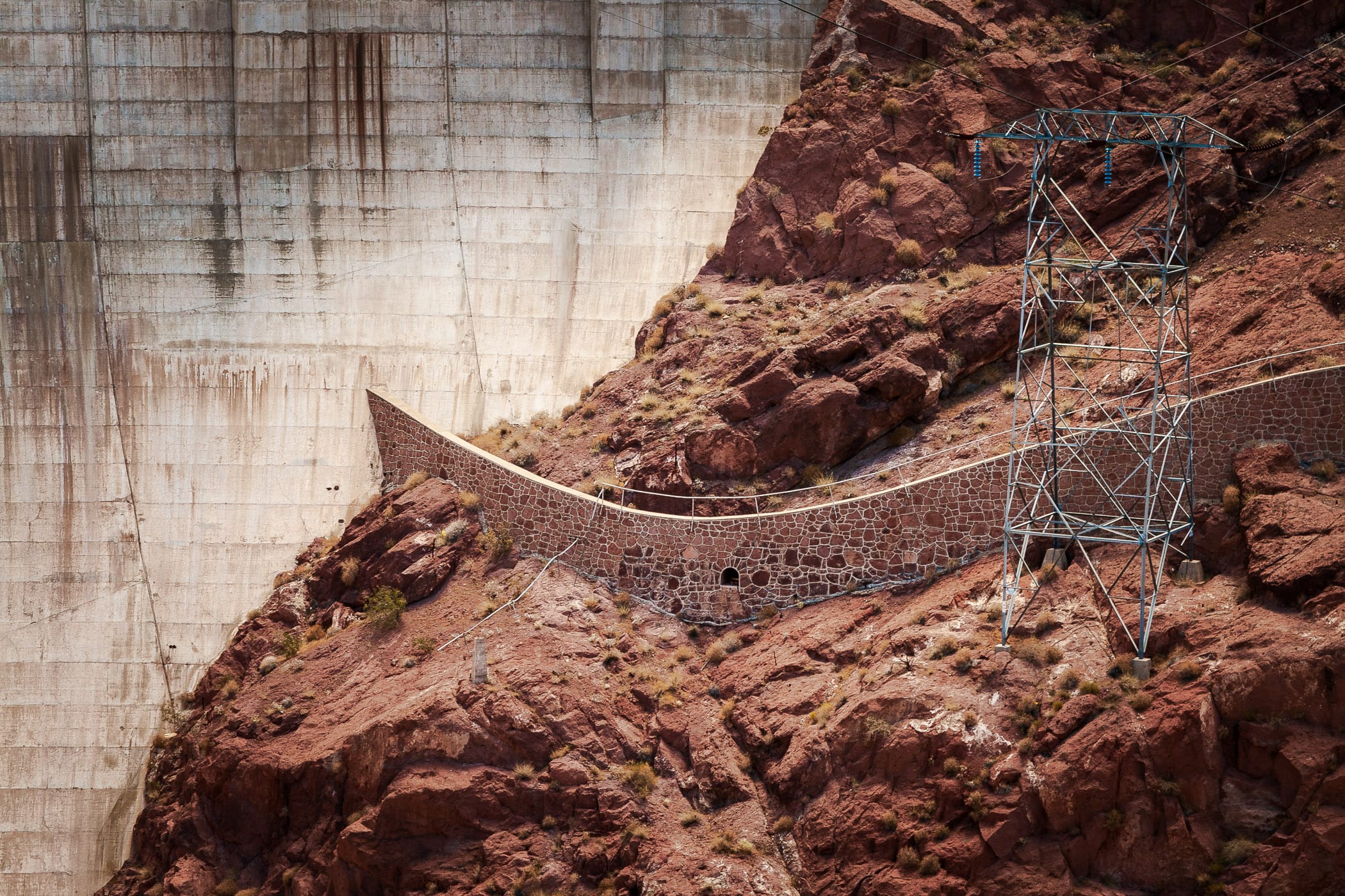A rock retaining wall and electrical tower next to downstream face of Hoover Dam.