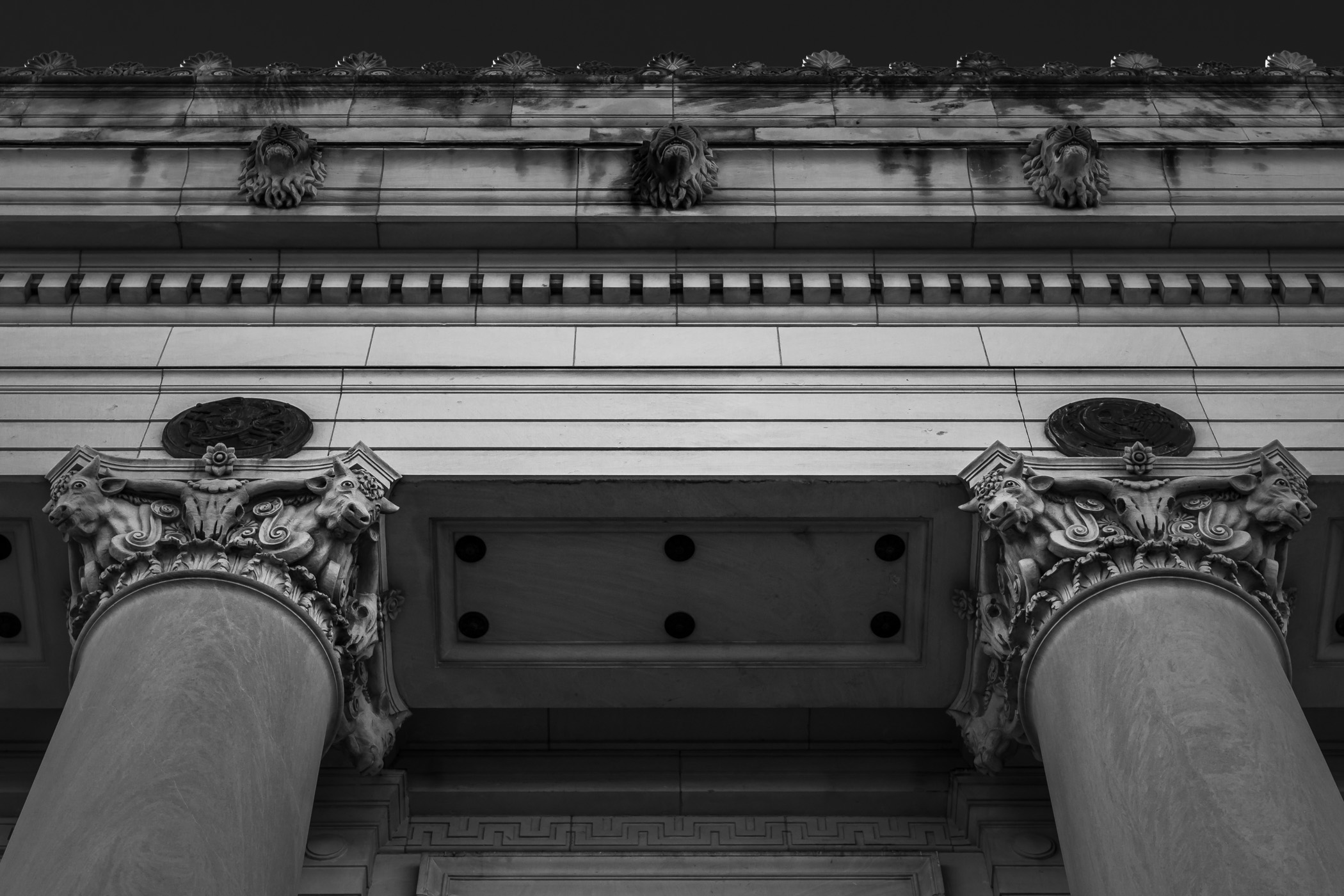 Exterior detail of the main post office in Fort Worth Texas, featuring lion heads along the frieze and various cow heads at the tops of the columns.