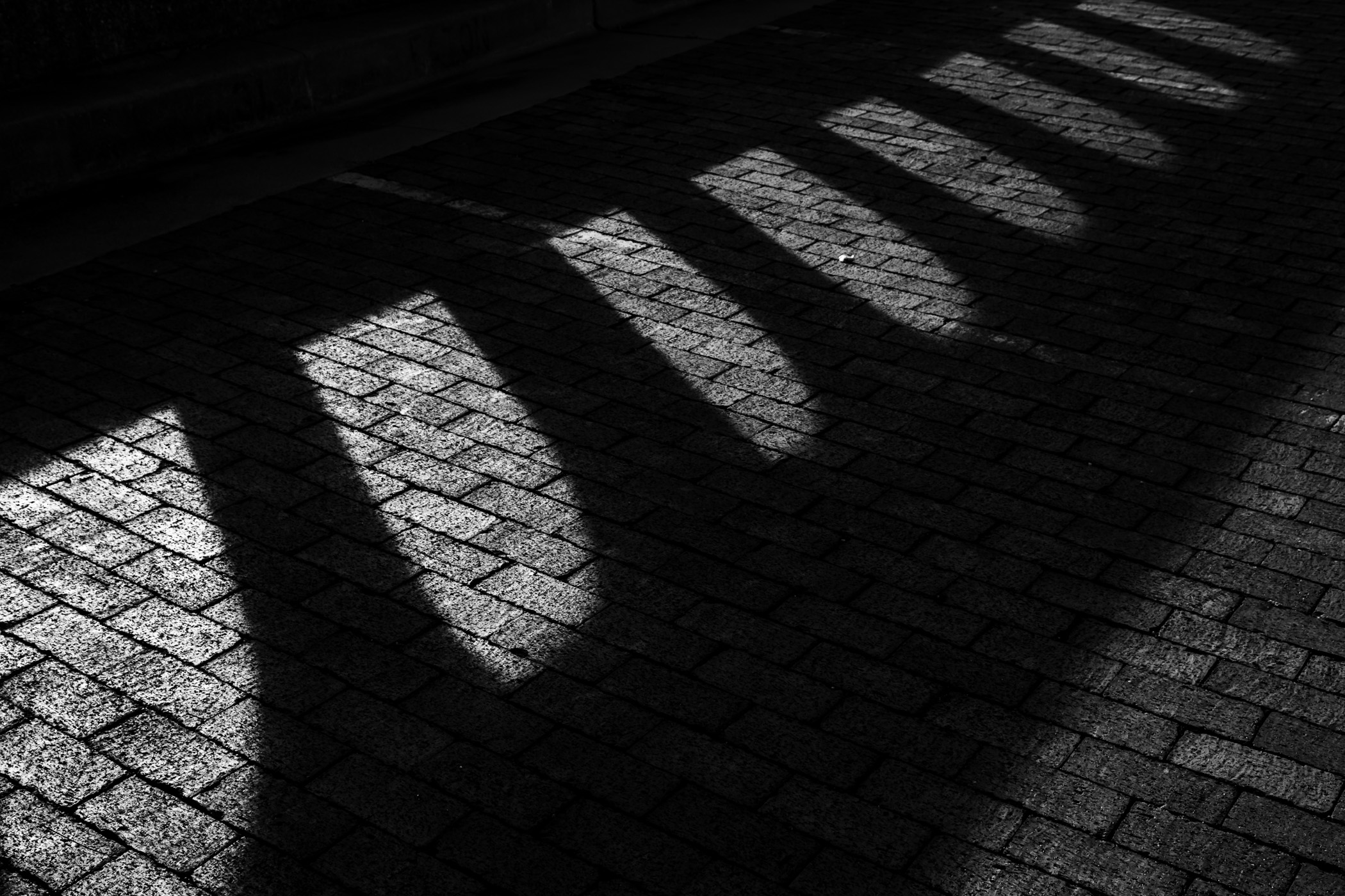 An old bridge's concrete railing casts a shadow on a brick street in Fort Worth, Texas.