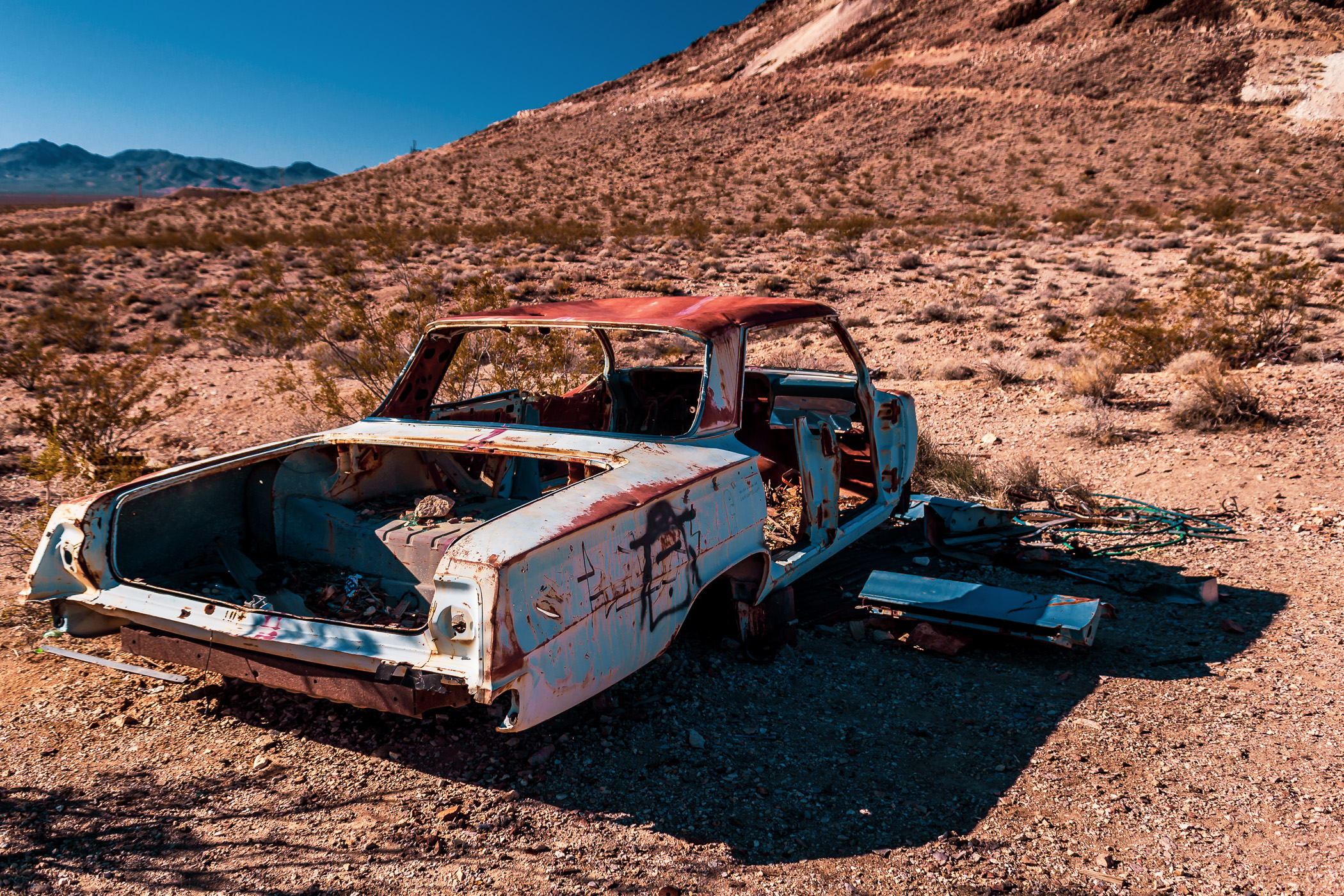 An abandoned Chevy Impala left to the elements in the middle of the vast, desolate Nevada desert near the border with California.