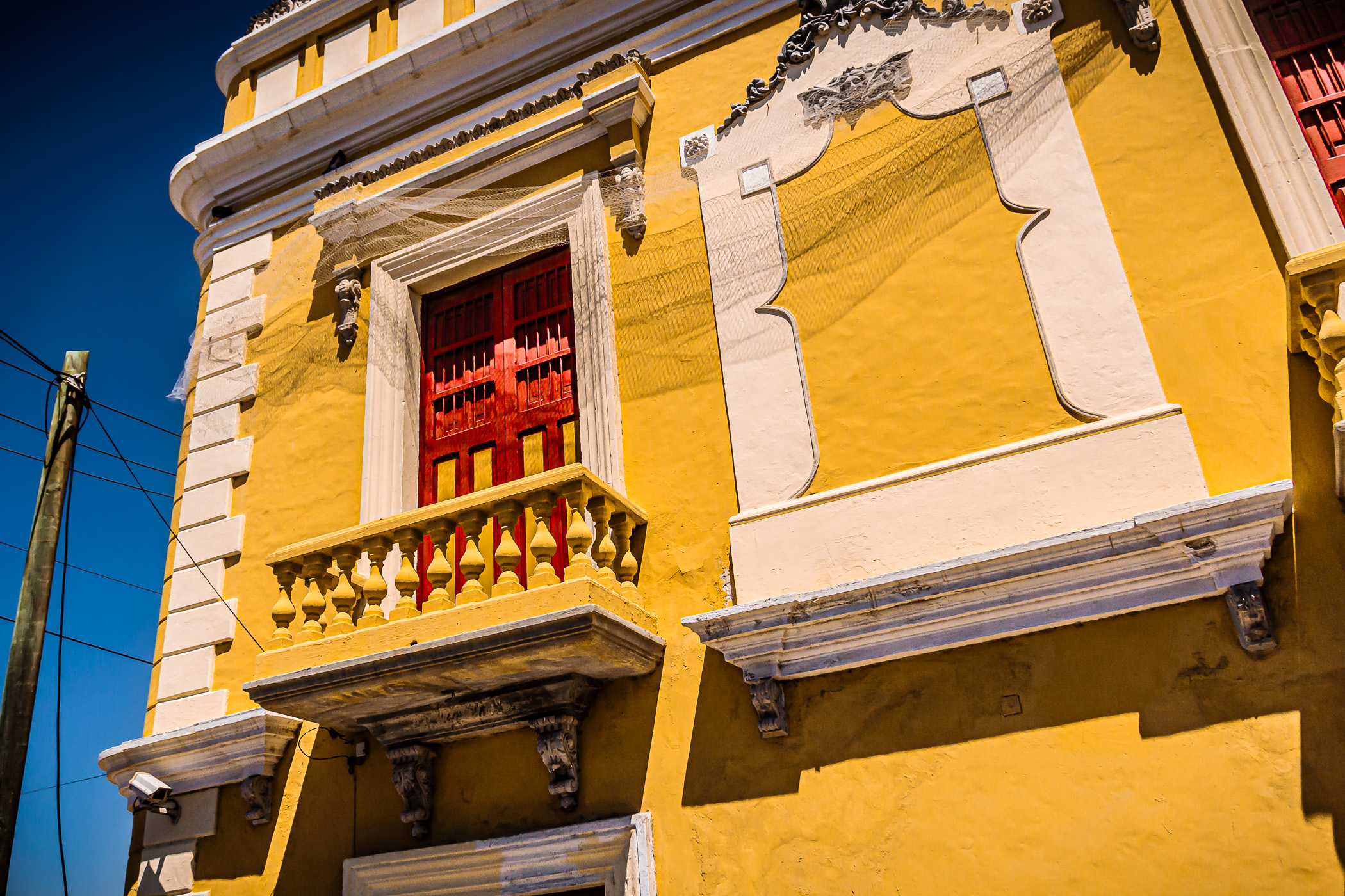 A red door on a balcony stands out against the yellow walls of its environs in Progreso de Mérida, Yucatan, Mexico.