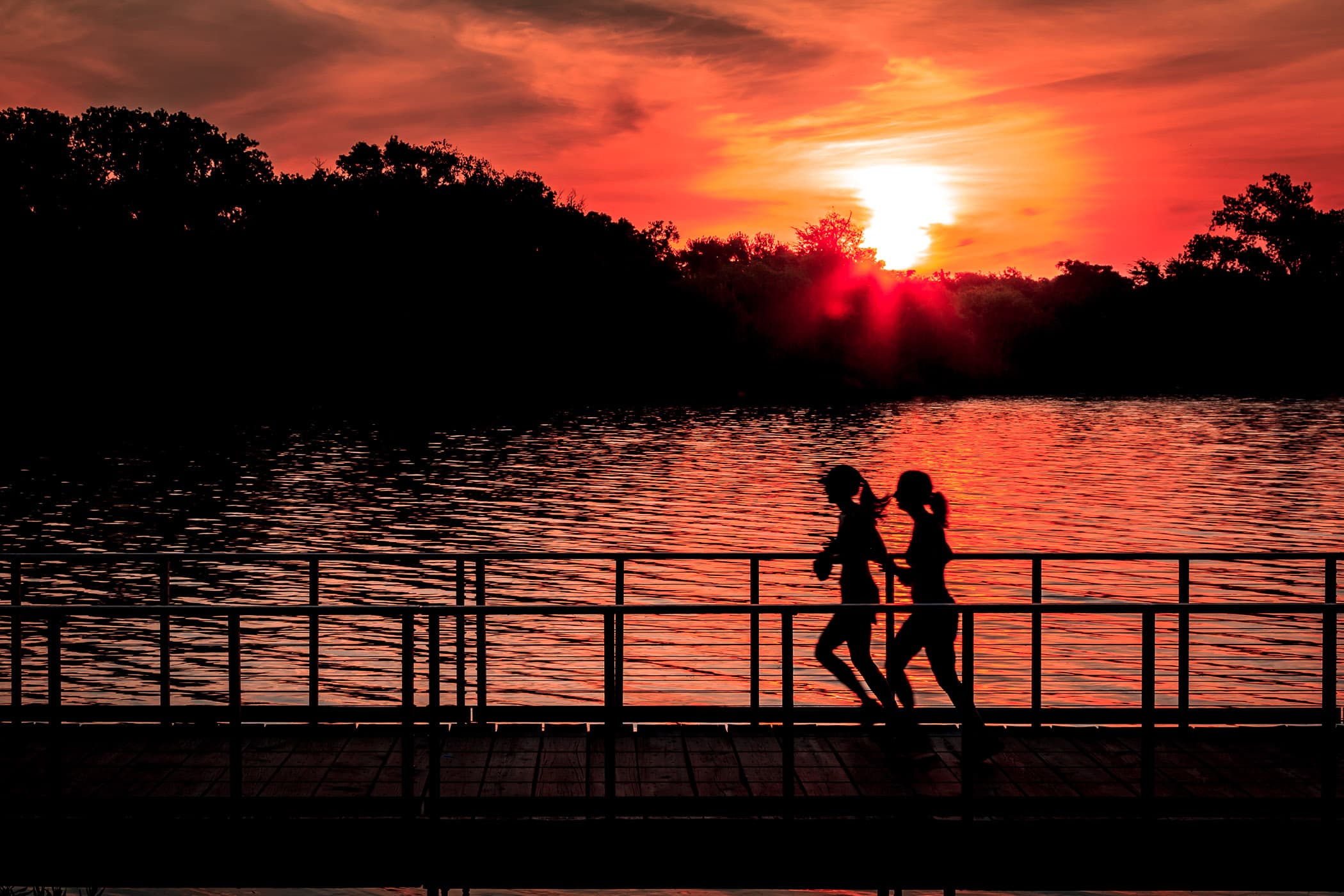 Joggers run along a footbridge as the sun rises over White Rock Lake, Dallas.