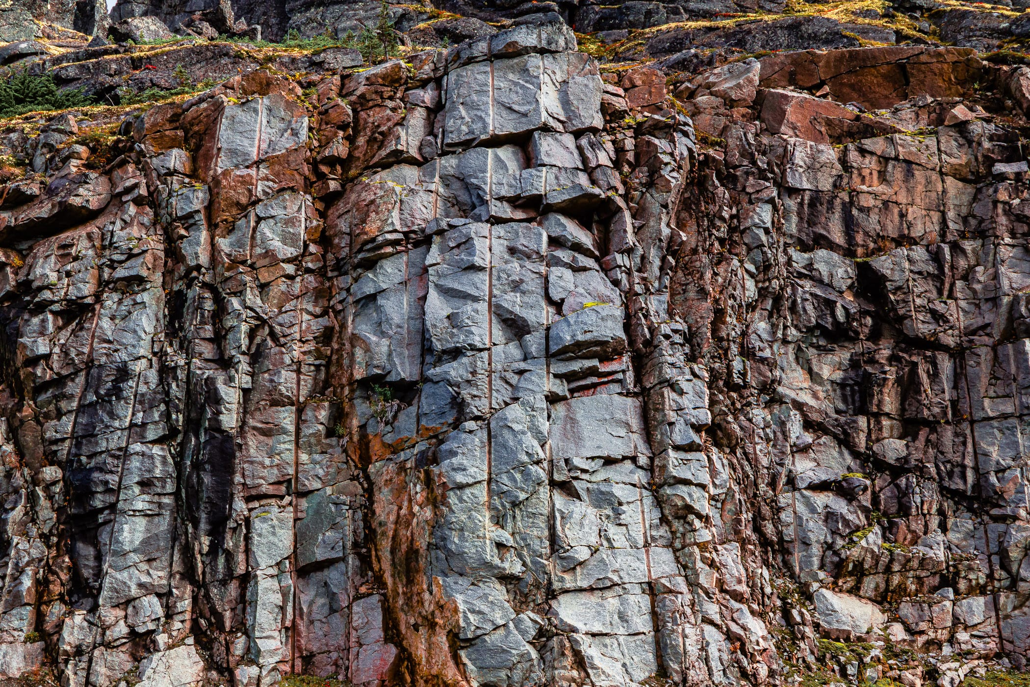 Cracked rocks showing vertical boreholes where explosives were placed to carve the Klondike Highway out of the rugged landscape of Alaska near the border with British Columbia, Canada.
