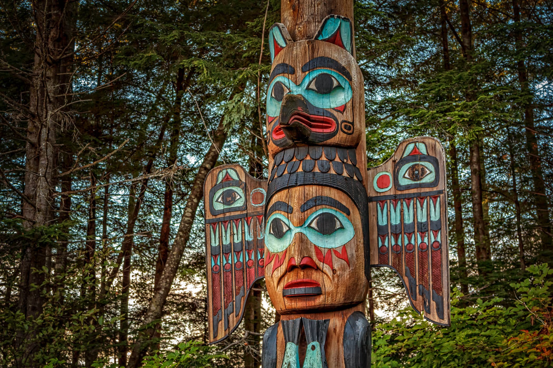 The Kadjuk Bird Pole at Ketchikan, Alaska's Totem Bight State Park depicts Raven forming the headdress of his wife, the Fog Woman, as she holds two salmon.