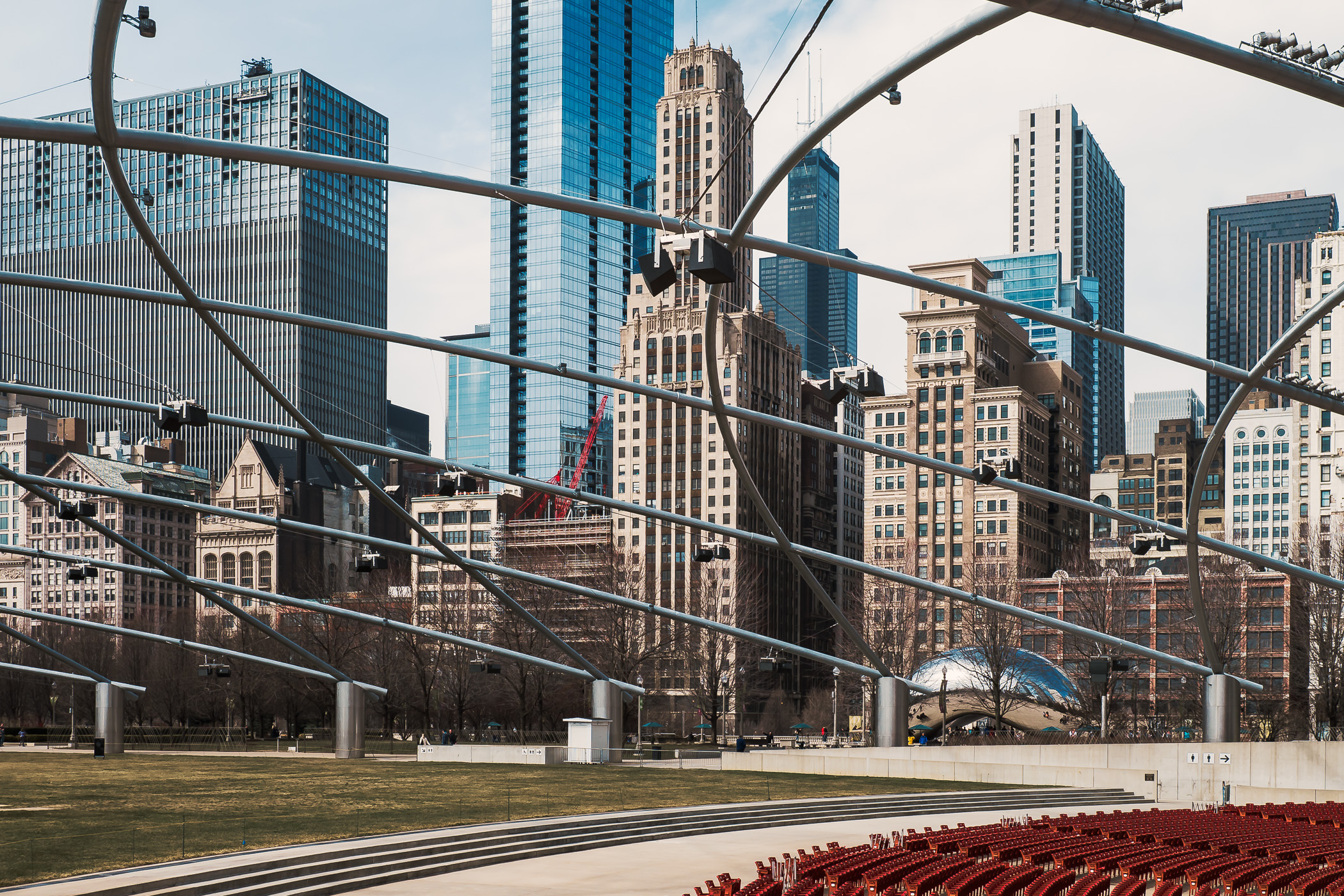 A view of part of the Chicago skyline through the overhead latticework of Millennium Park’s Jay Pritzker Pavillion. In the distance, the silver sculpture Cloud Gate (or "The Bean") can be seen.