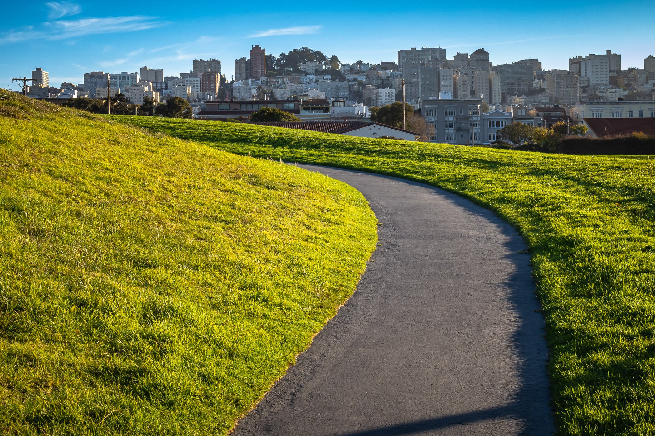 A path crests a hill in the Great Meadow at Fort Mason as the late afternoon sun begins to set on San Francisco.