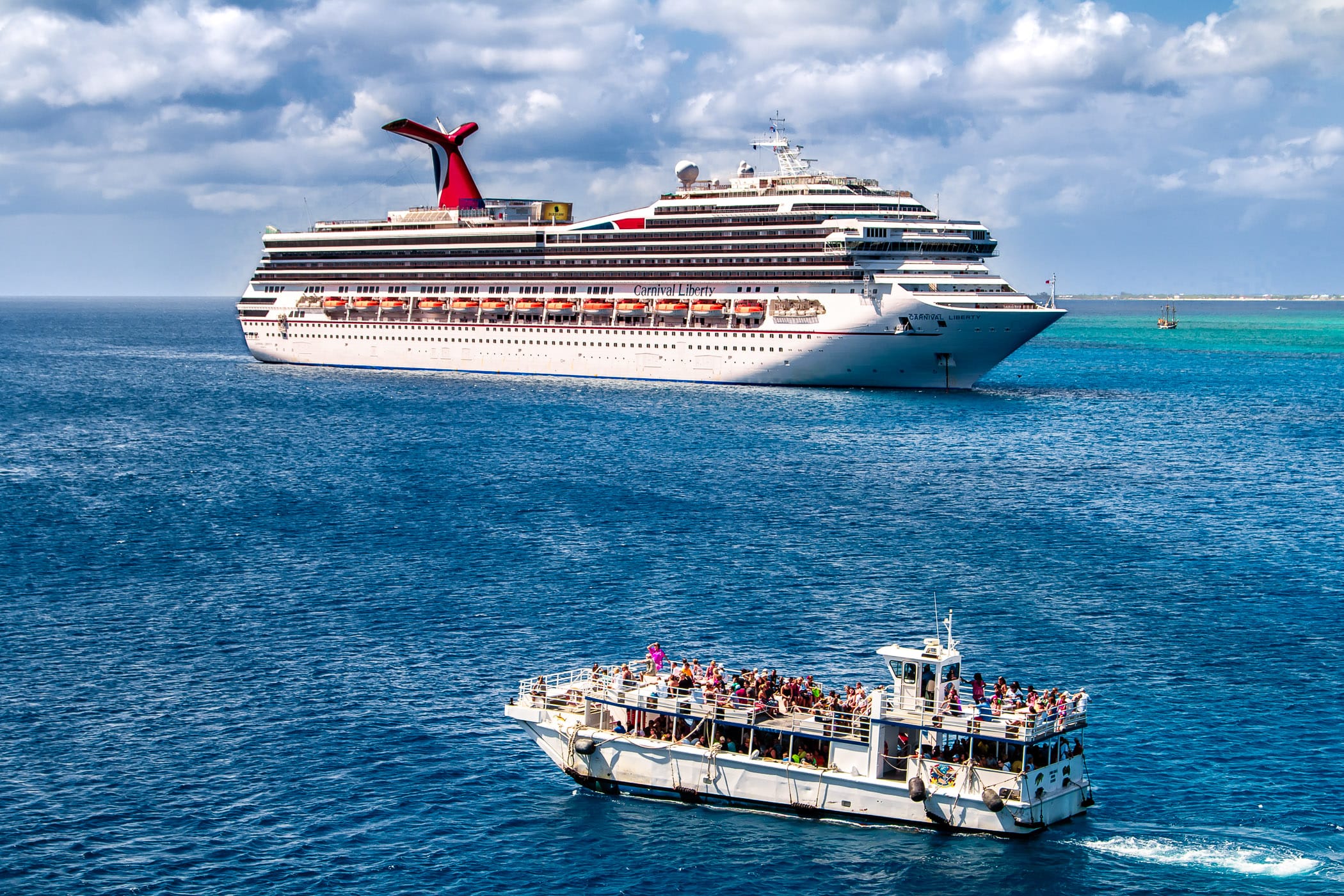A cruise ship tender—used to transport passengers between a port and a ship when the ship is unable to dock directly due to shallow water or other reasons—passes the Carnival Liberty just off the coast of George Town, Grand Cayman.