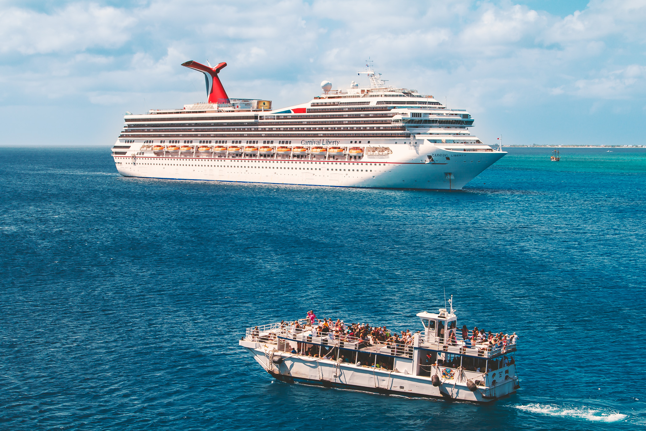 A cruise ship tender—used to transport passengers between a port and a ship when the ship is unable to dock directly due to shallow water or other reasons—passes the Carnival Liberty just off the coast of George Town, Grand Cayman.