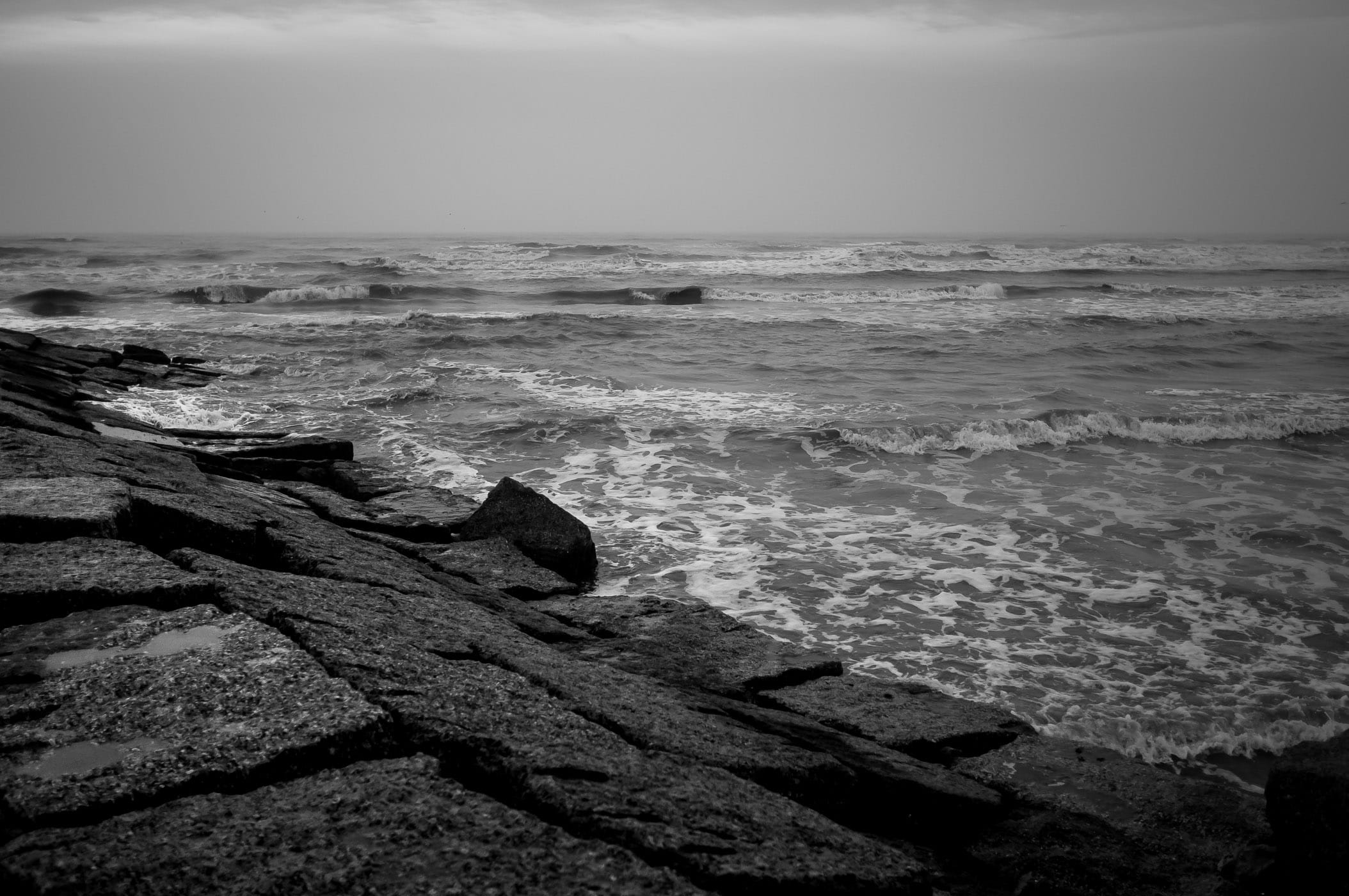 Waves crash against a granite groyne on an overcast day at Galveston Island, Texas.
