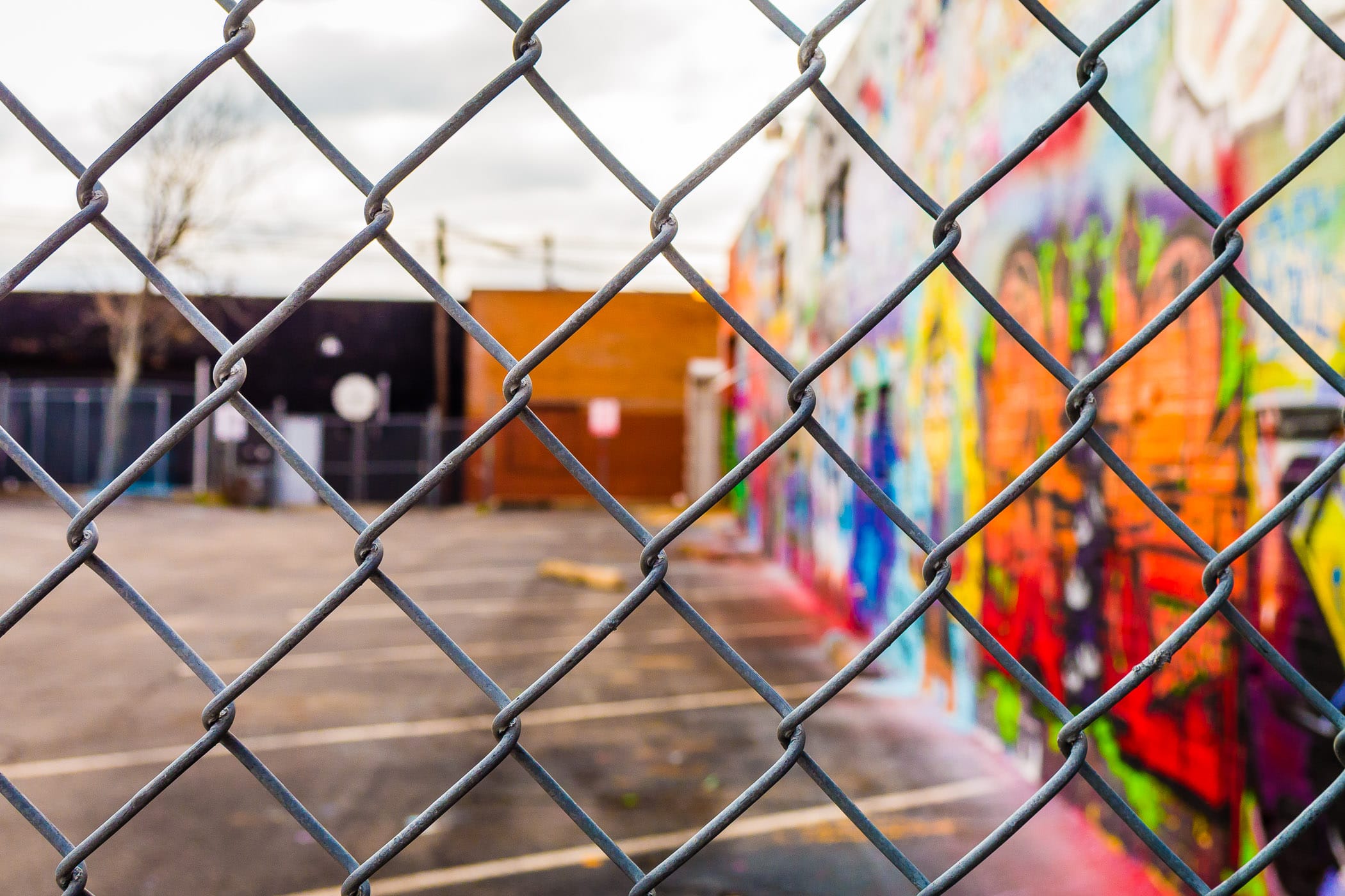 A wall covered with a graffiti mural adjacent to a fenced-in parking lot in Dallas' Deep Ellum neighborhood.