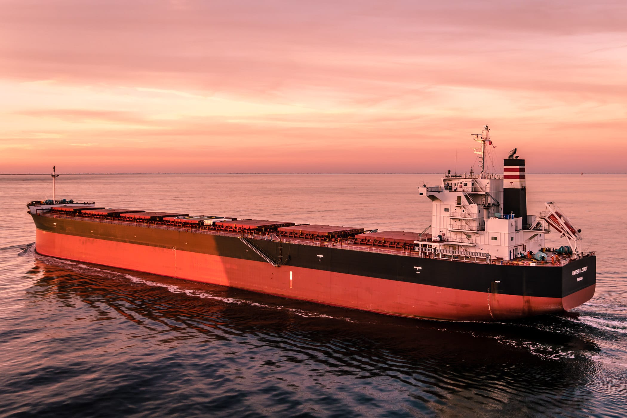 The bulk carrier United Legacy transits Bolivar Roads just off the coast of Galveston, Texas, as the sun sets on the Gulf of Mexico.