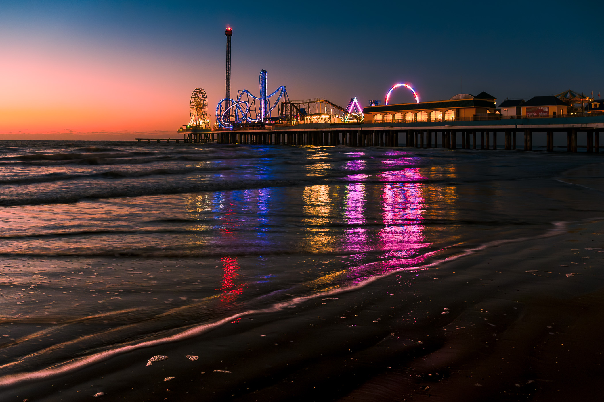 The first light of day rises on the Gulf of Mexico as the lights from Galveston, Texas' Historic Pleasure Pier reflect on the surf.