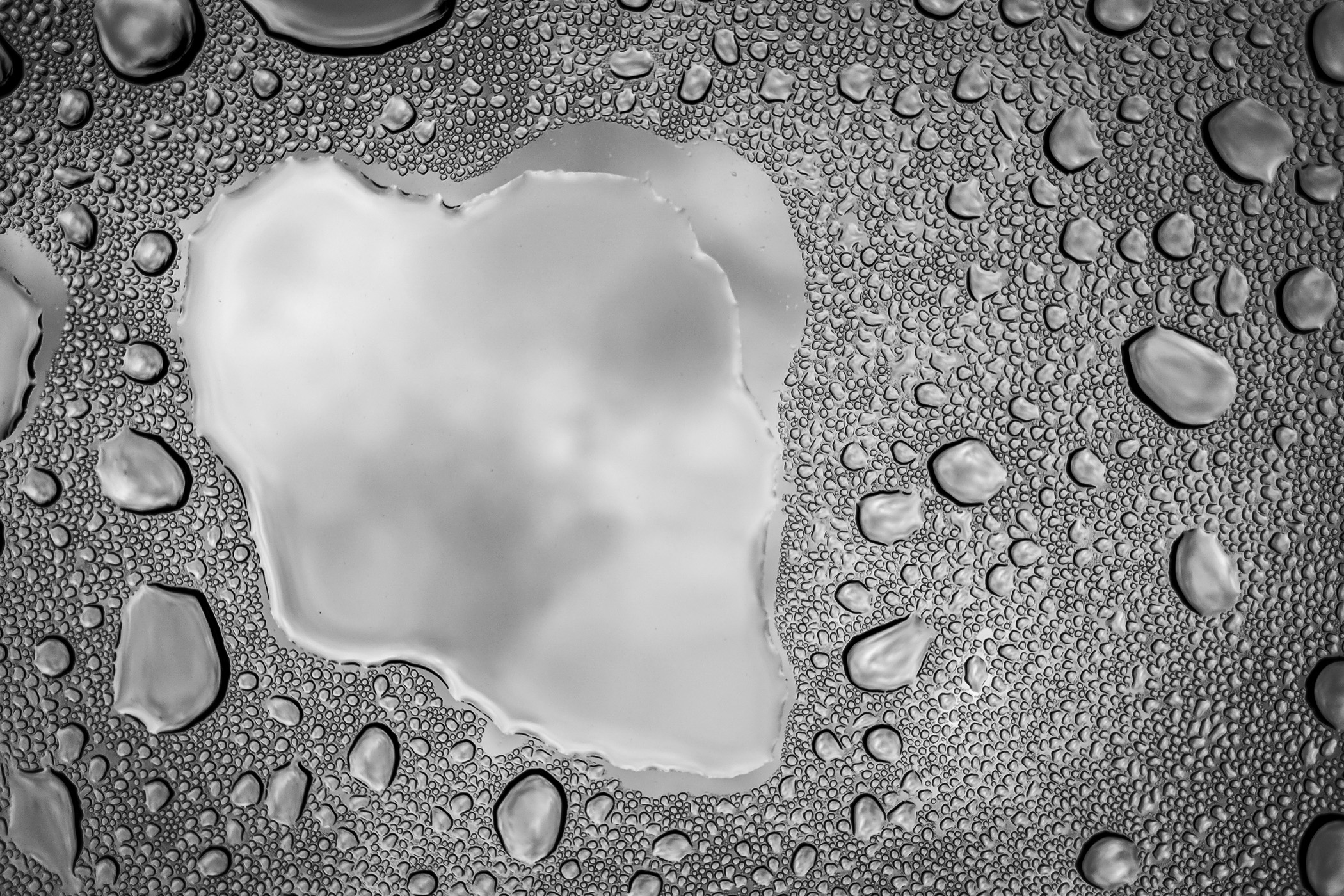 Rain drops on a car's sunroof form a portal to the cloudy sky above.