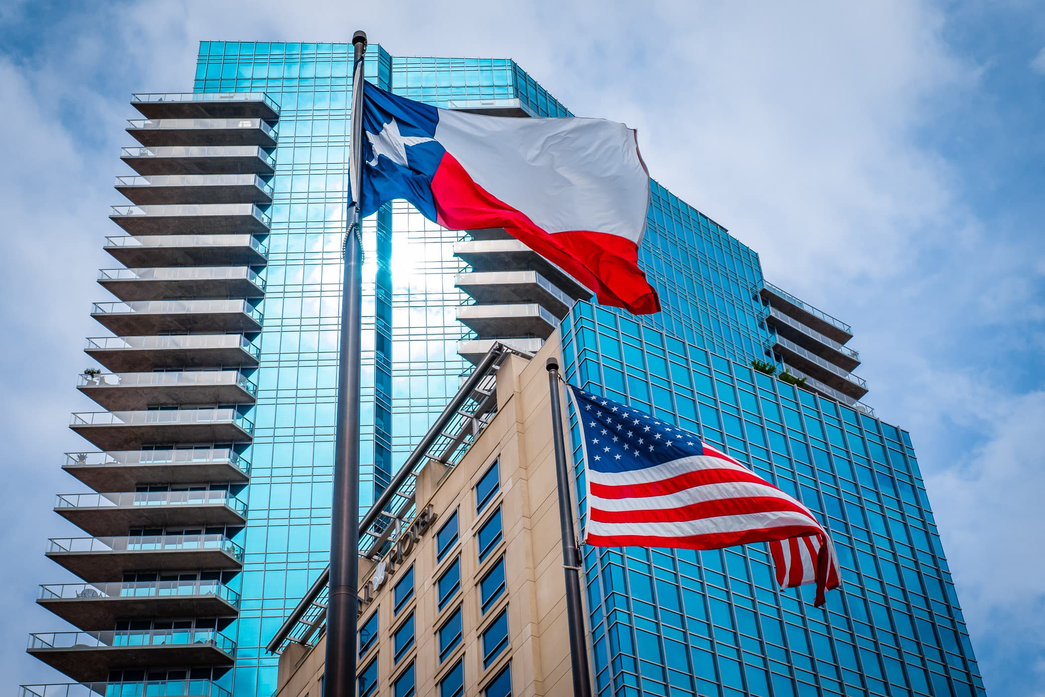 The Omni Fort Worth Hotel rises above the Texas Flag and the United States Flag.