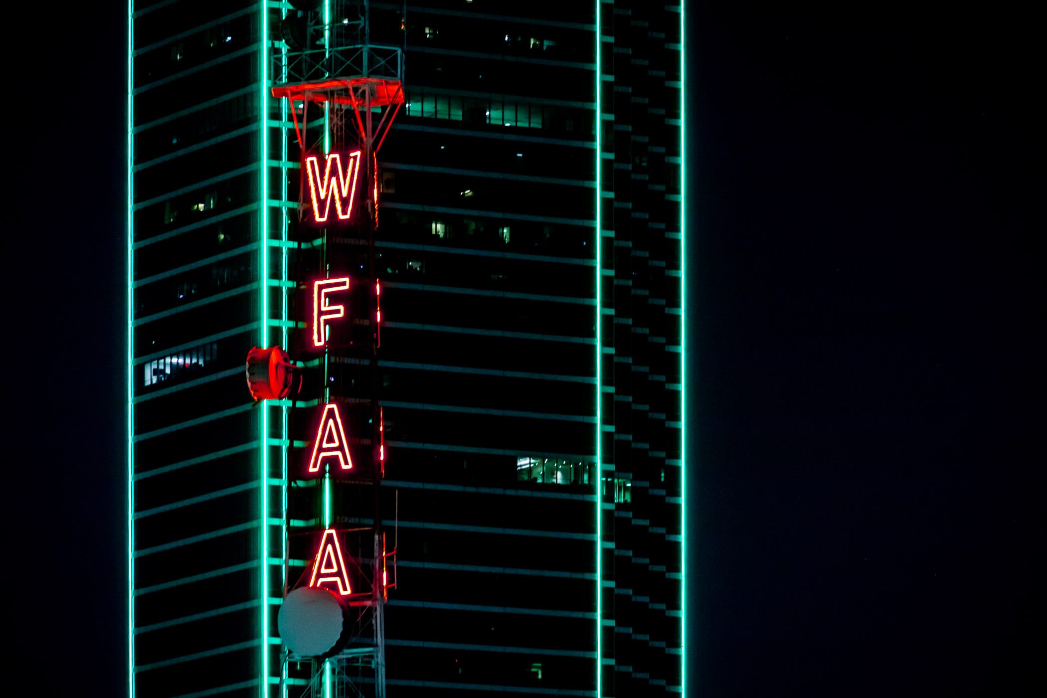 A broadcast tower at WFAA glows in Dallas' night sky near Bank of America Plaza.