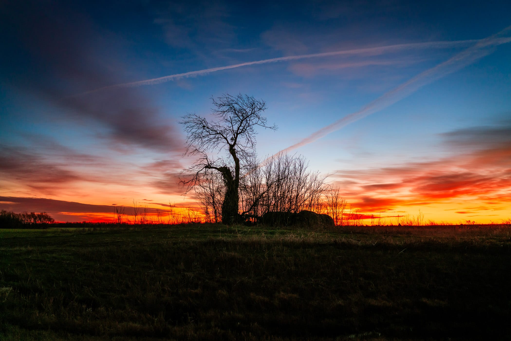 The sun rises on a tree and nearby bales of hay near Dorchester, Texas.