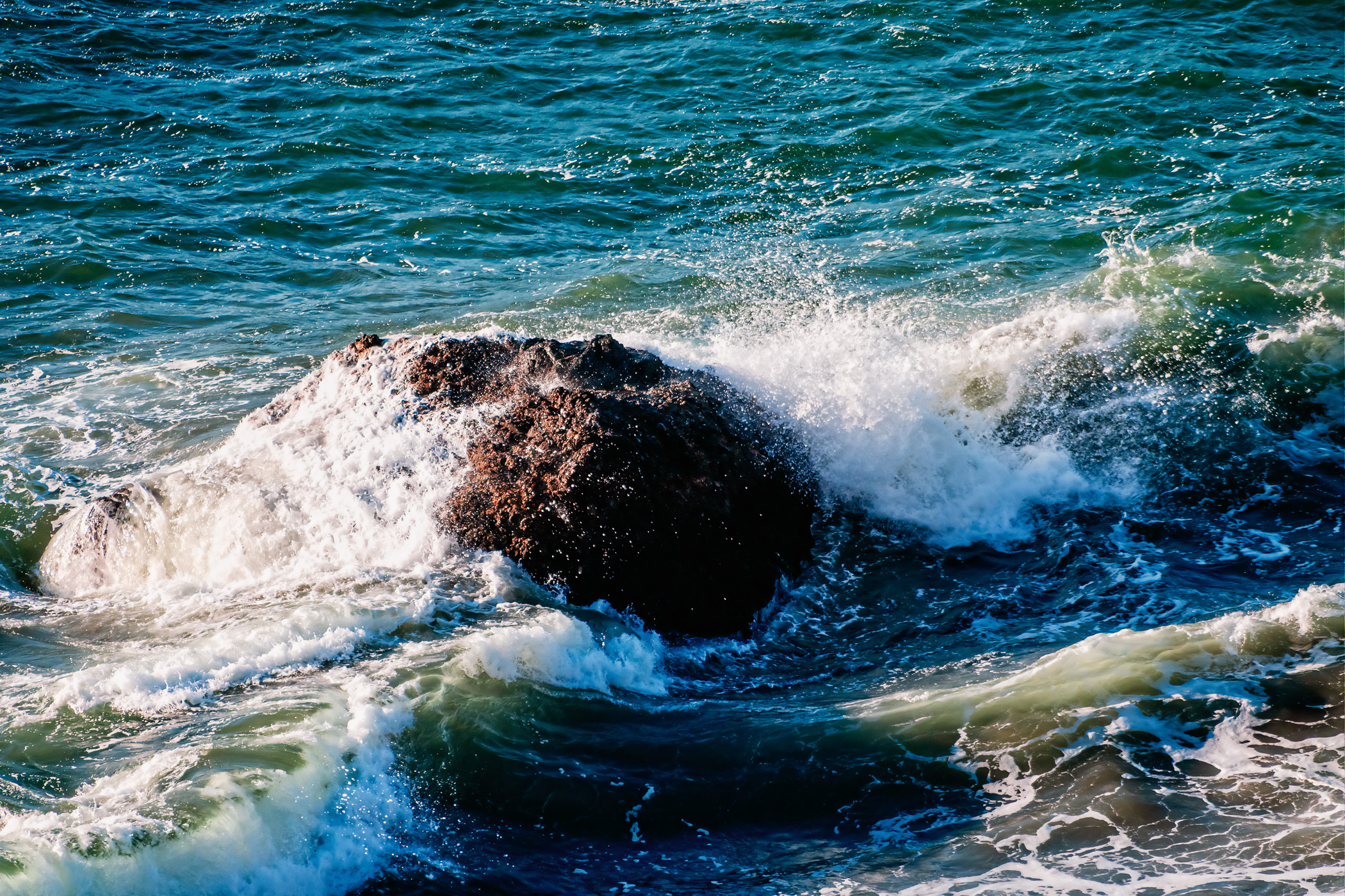 Waves crash over a rock along the Pacific Ocean shoreline at Lands End, San Francisco.