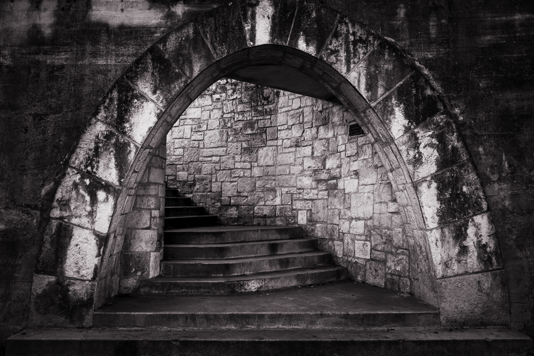 A stairwell is framed by a stone arch along the historic San Antonio Riverwalk, Texas.