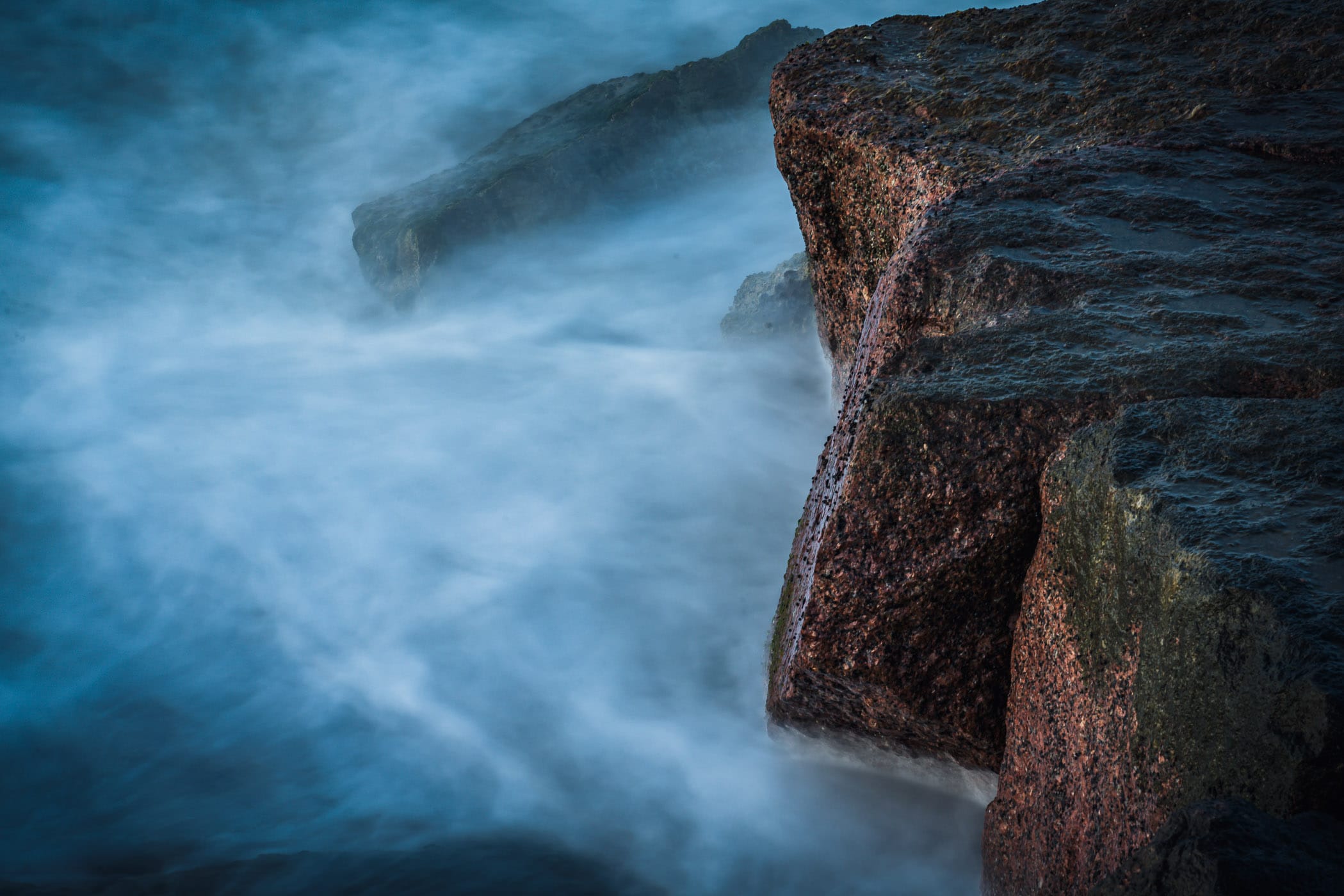 A long exposure shot of waves on granite erosion-control blocks along the Galveston, Texas, beach.