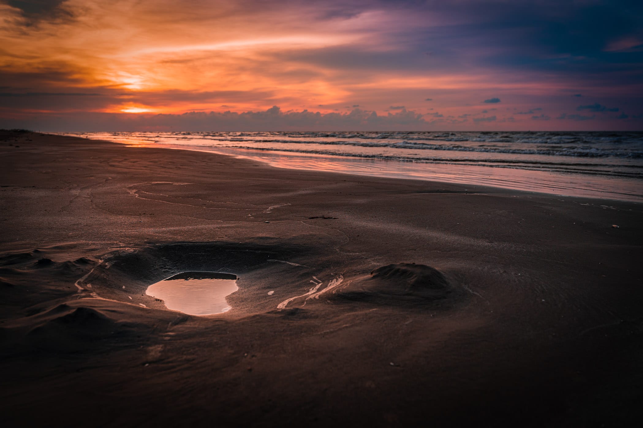 A puddle on a Galveston, Texas, beach greets the rising sun.