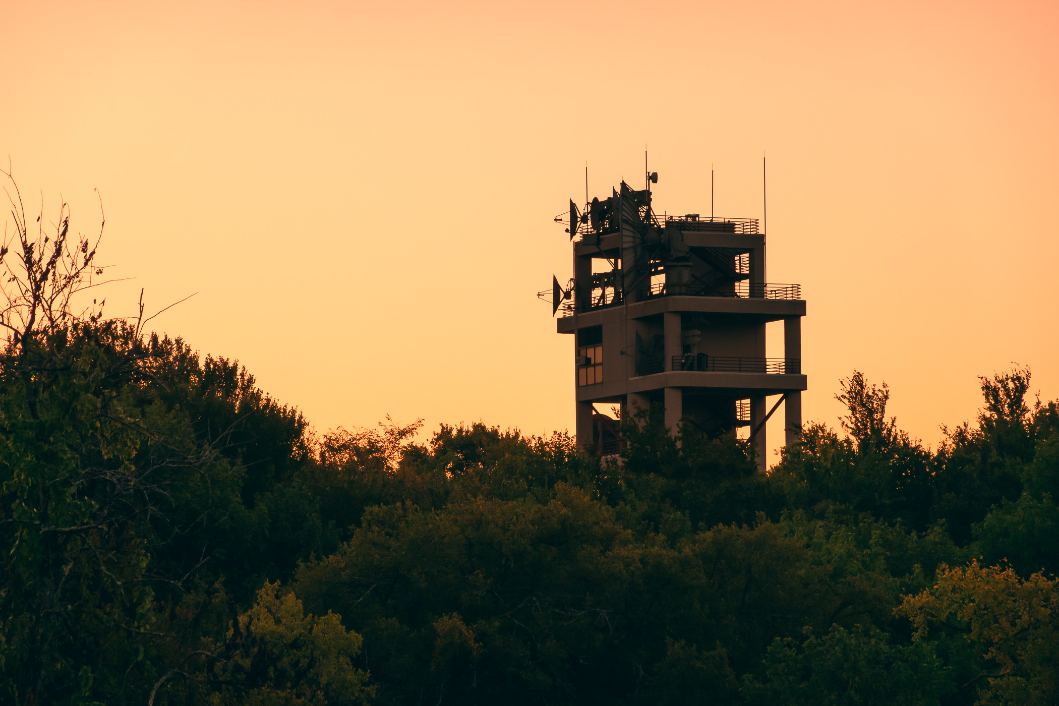 The rising sun silhouettes a mysterious tower covered in communications equipment at Raytheon Intelligence & Space, McKinney, Texas.