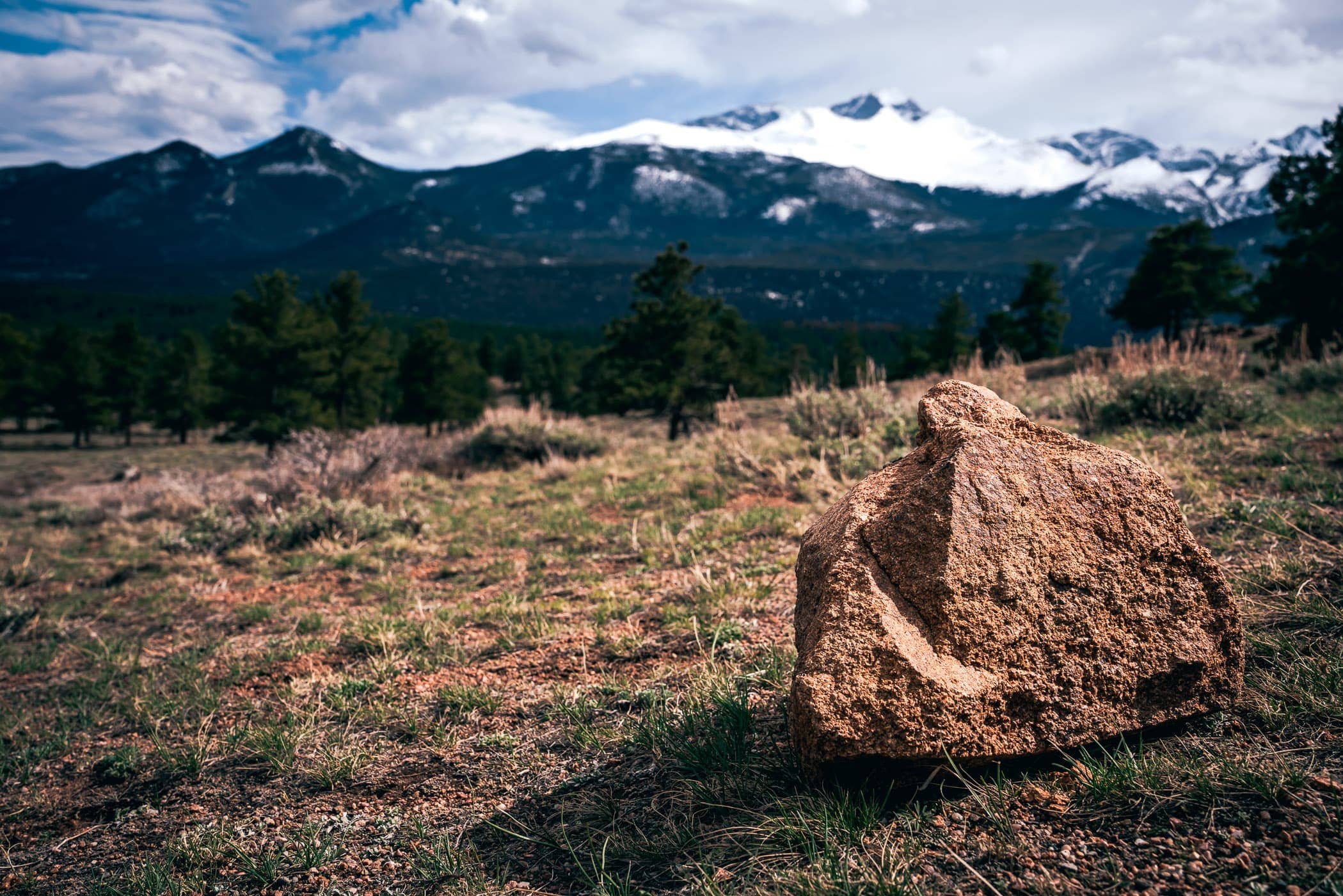 Snow-capped mountains loom over a rock at Colorado's Rocky Mountain National Park.
