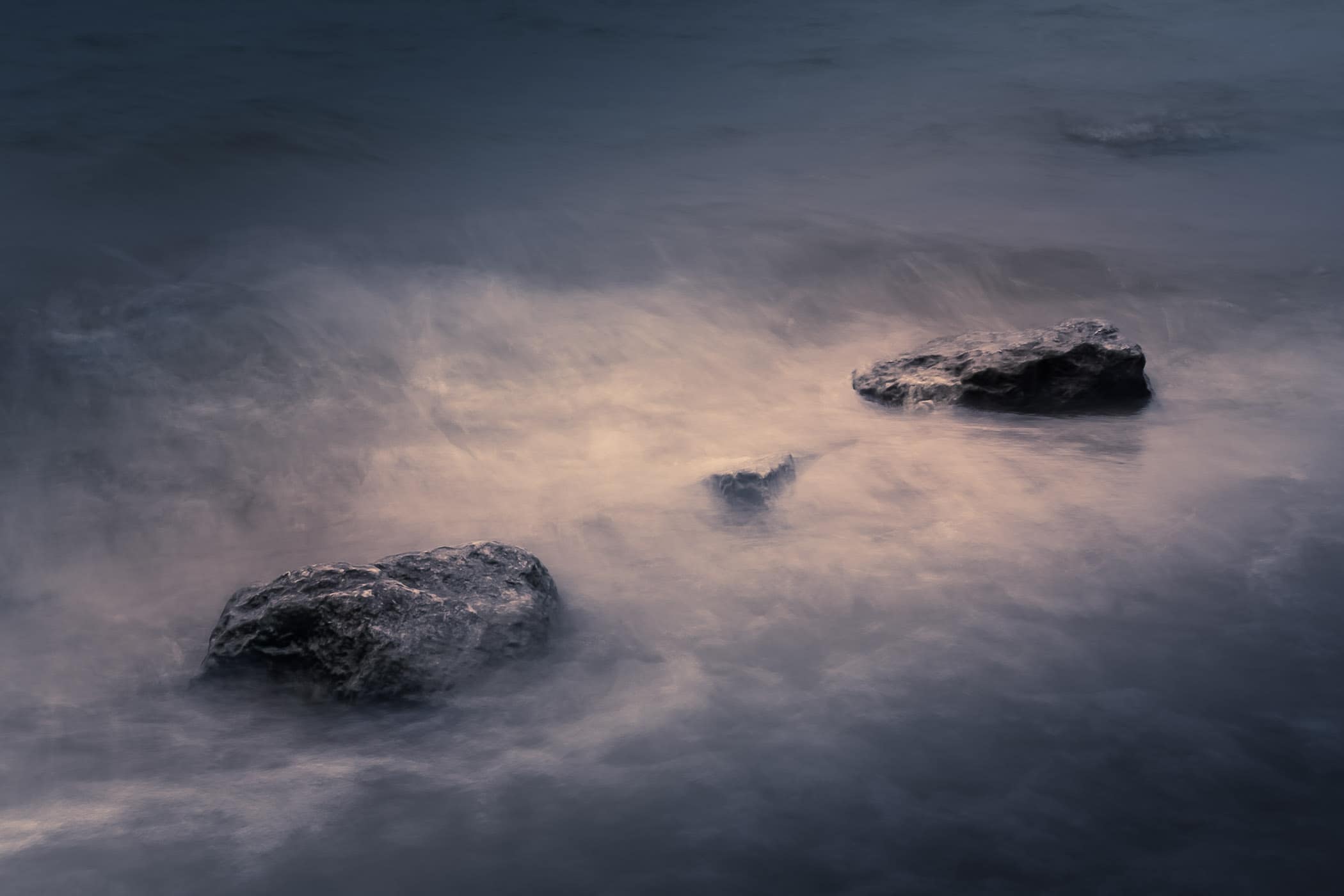Three rocks on the shore of North Texas' Lake Lavon are washed over by waves.