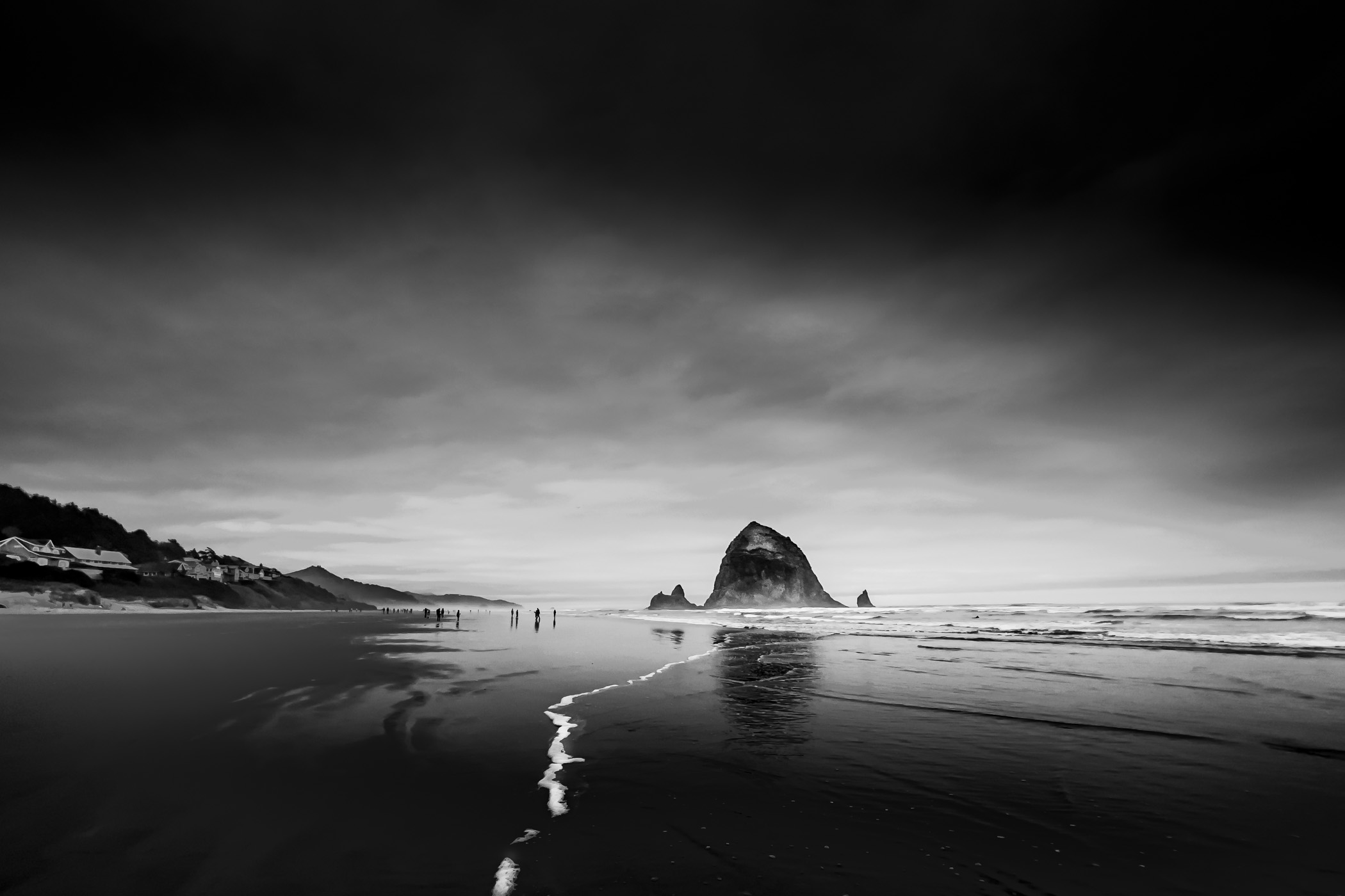 Haystack Rock looms over beachgoers at Cannon Beach, Oregon, on a cold early-Spring day.