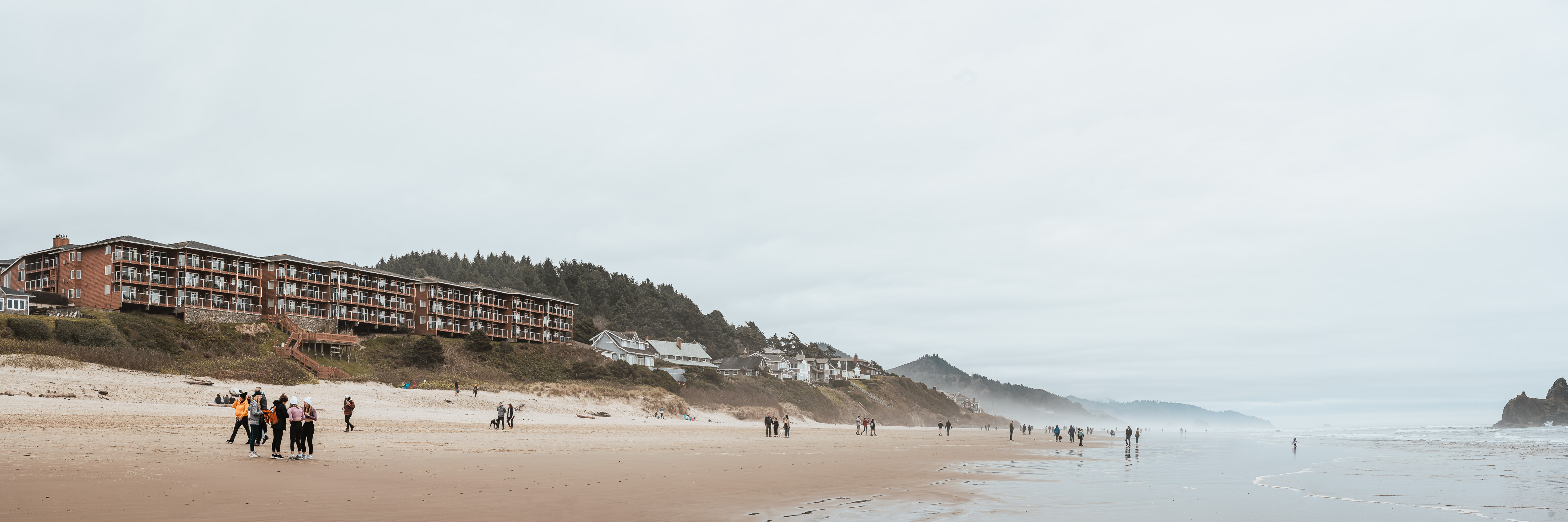 Visitors walk Oregon's Cannon Beach on a cold, overcast, late-winter day.