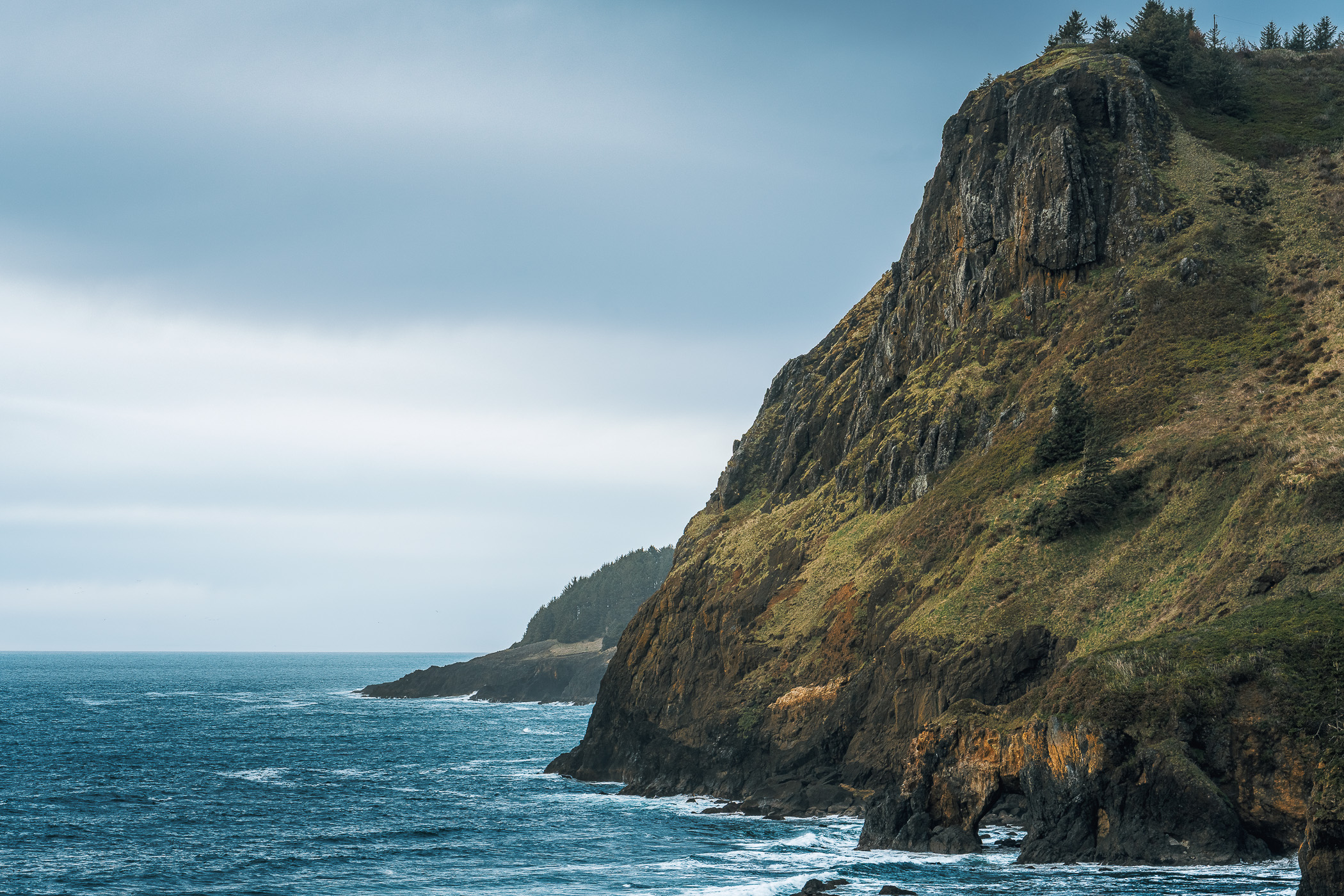 The rugged cliffs of Oregon's Otter Rock State Scenic Viewpoint overlook the Pacific Ocean on a gloomy day.