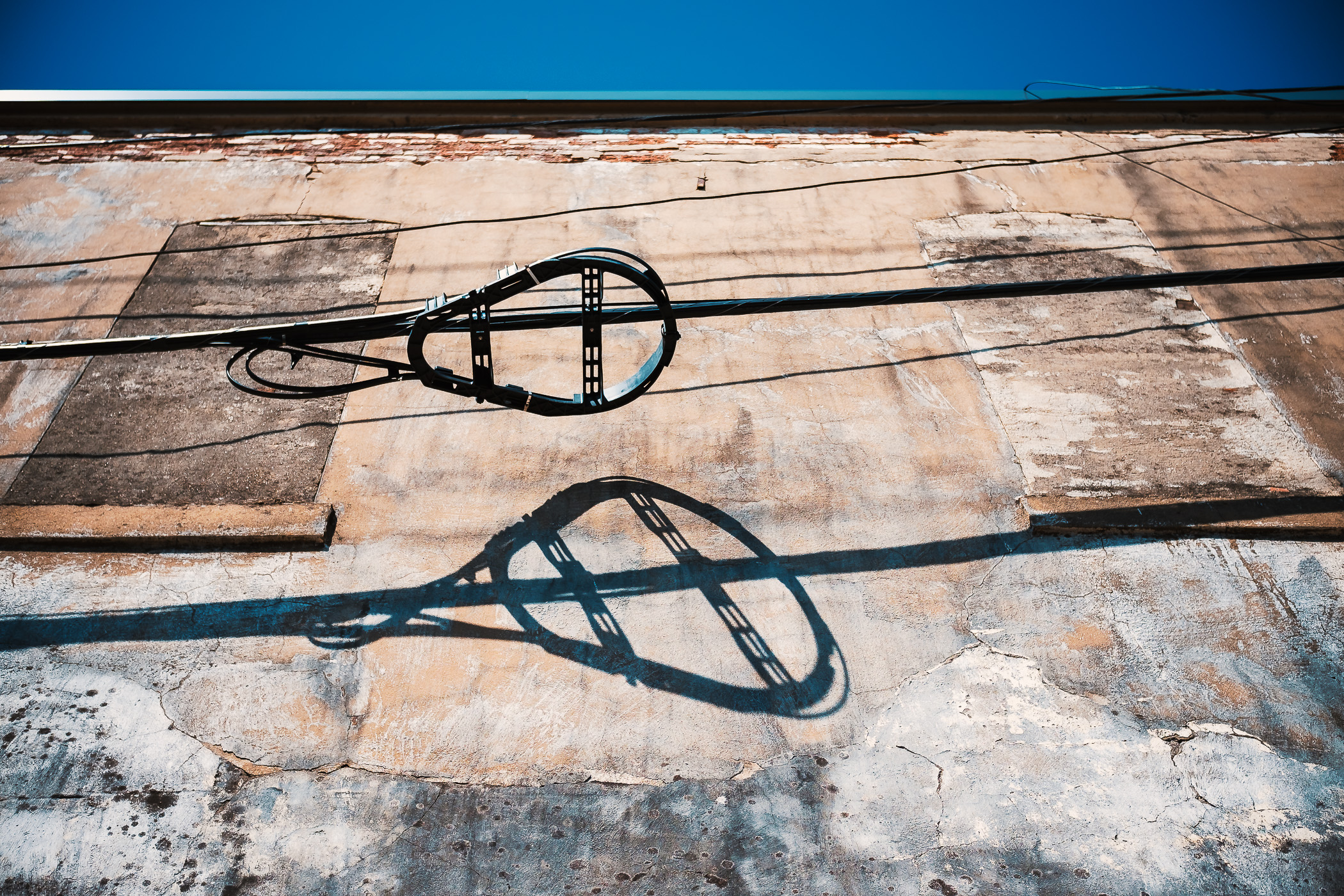A device for storing excess slack in a fibre optic cable—colloquially known as a "snowshoe"—casts a shadow on an adjacent building in Downtown McKinney, Texas.